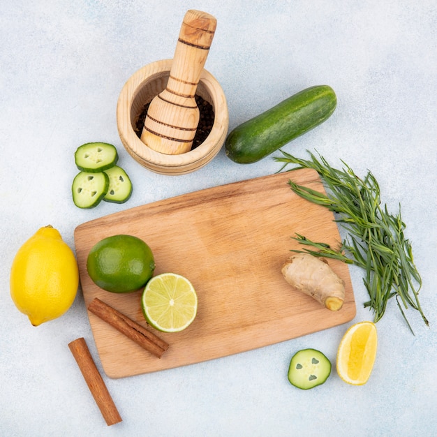 Top view of fresh lemons on wood kitchen board with cinnamon sticks and ginger with tarragon greens on white