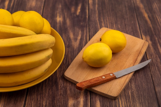 Top view of fresh lemons on a wooden kitchen board with knife with lemons on a yellow plate with bananas on a wooden surface