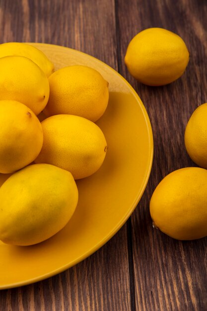 木製の壁に隔離されたレモンと黄色のプレート上の新鮮なレモンの上面図