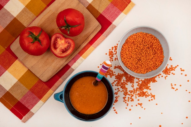 Vista dall'alto di lenticchie fresche su una ciotola con zuppa di lenticchie arancione su una ciotola con pomodori su una tavola da cucina in legno su un panno controllato su sfondo bianco