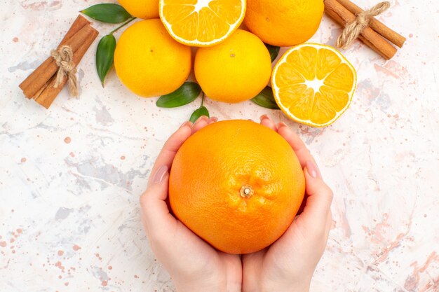 Top view fresh mandarines cinnamon sticks orange in woman hands on bright isolated surface