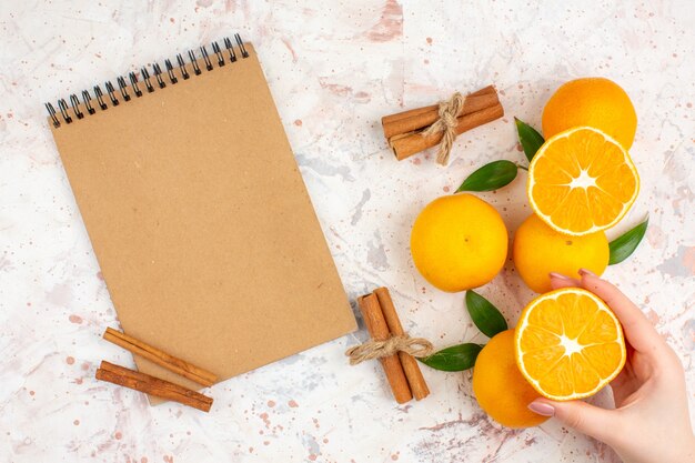 Top view fresh mandarines notebook cinnamon sticks cut mandarine in woman hand on bright isolated surface