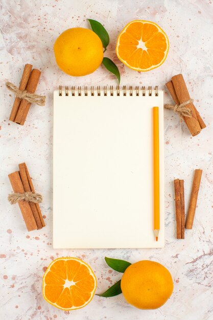 Top view fresh mandarines notepad pencil cinnamon sticks on bright isolated surface