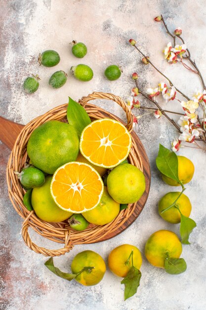 Top view fresh mandarines in wicker basket on a cutting board feykhoas apricot blossom branch on nude background