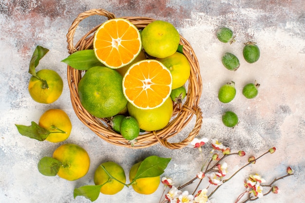 Top view fresh mandarines in wicker basket surrounded by mandarines feykhoas on nude background