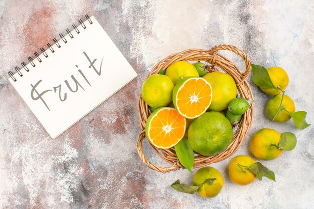 Top view fresh mandarines in wicker basket surrounded by mandarines fruit written on notebook on nude background