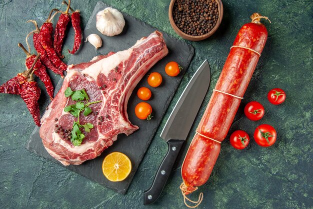Вид сверху ломтик свежего мяса с оранжевыми помидорами и колбасой на темно-синем фоне цвет еда мясо кухня животное курица корова мясник