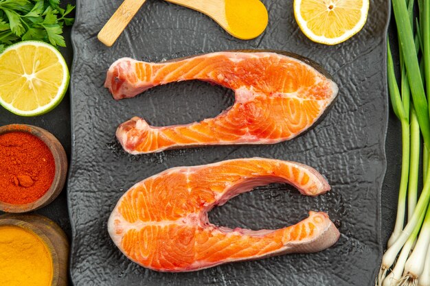 Top view fresh meat slices with greens lemon and seasonings on a dark background