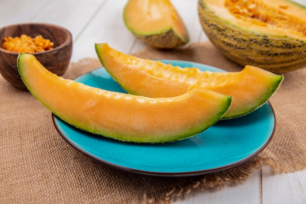 Top view of fresh melons on blue plate on sack cloth with seeds on wood bowl on white