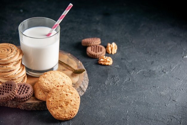 Top view of a fresh milk in a glass various cookies and walnuts on the wooden board on the right side on black background