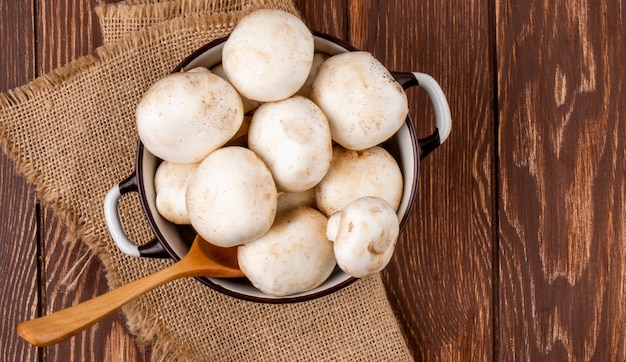 Top view of fresh mushrooms champignon in a pan on wooden rustic background