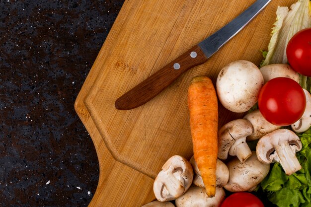 Top view of fresh mushrooms champignon with a knife and fresh vegetables on a wooden board