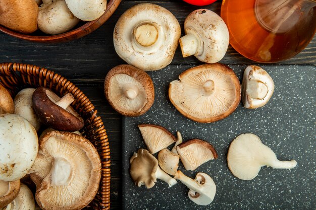 Top view of fresh mushrooms in a wicker basket and on a black cutting board on dark wood