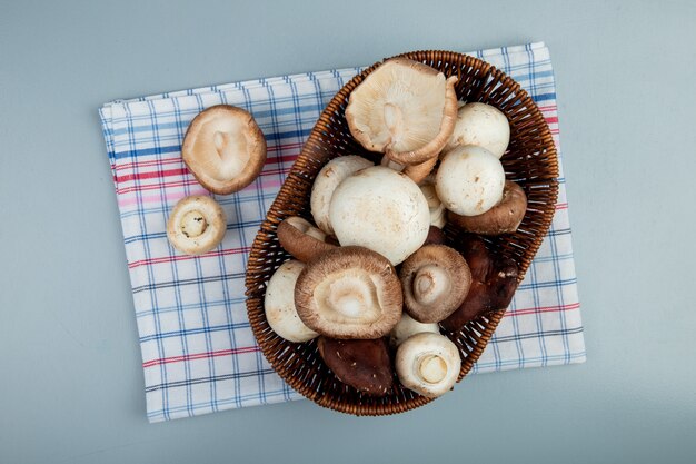 top view of fresh mushrooms in a wicker basket on plaid napkin on light blue surface