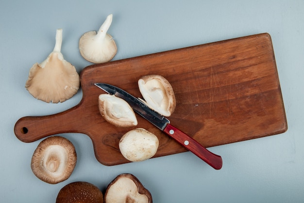 Top view of fresh mushrooms on a wood cutting board with kitchen knife on light blue