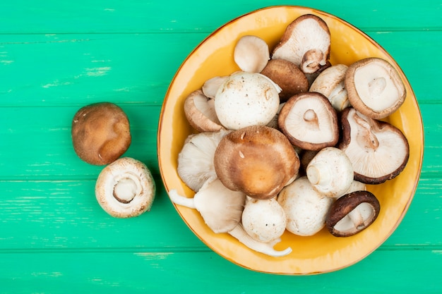 top view of fresh mushrooms on a yellow plate on green wooden surface