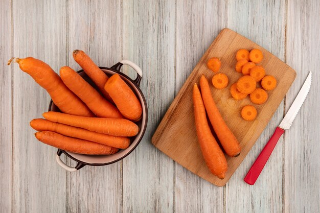 Top view of fresh orange carrots on a wooden kitchen board with knife with carrots on a bowl on a grey wooden surface