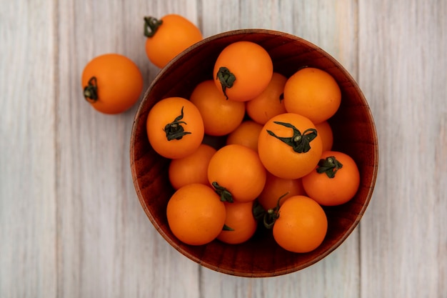 회색 나무 표면에 나무 그릇에 신선한 오렌지 체리 토마토의 상위 뷰