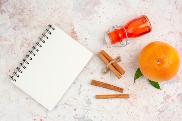 Top view fresh orange cinnamon sticks bottle a notebook on bright surface