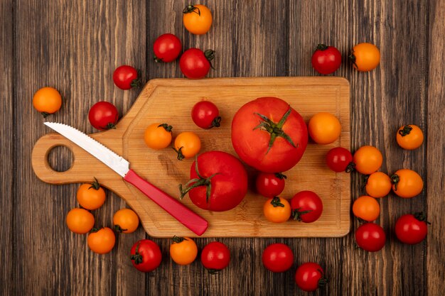 木製の壁にナイフで木製のキッチンボードに分離された新鮮なオレンジと赤のトマトの上面図
