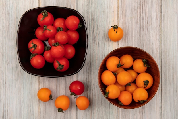 Top view of fresh orange tomatoes on a wooden bowl with red tomatoes on a black bowl on a grey wooden wall