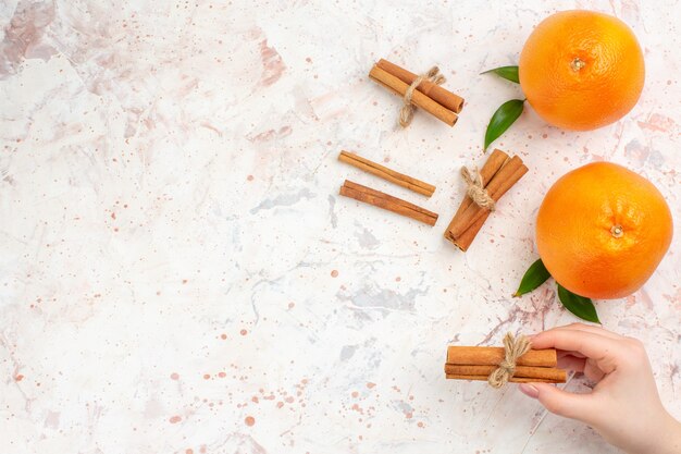 Top view fresh oranges cinnamon sticks in female hand on bright surface with copy space