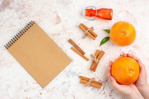 Бесплатное фото Вид сверху свежие апельсины палочки корицы апельсин в женской руке бутылку записной книжки на яркой поверхности