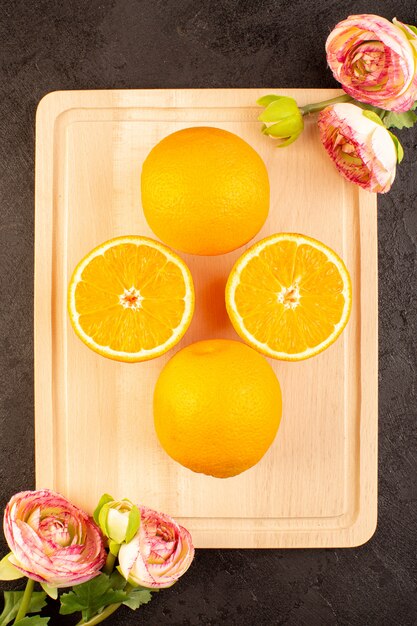 A top view fresh oranges sour ripe whole and sliced with dried roses mellow citrus tropical vitamine yellow on the dark desk