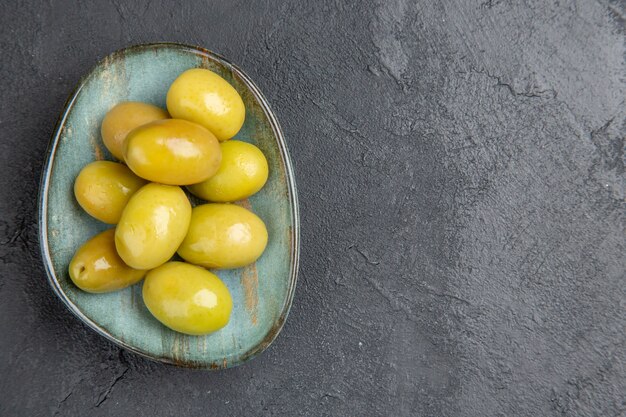 Top view fresh organic green olives on a blue plate on the right side on a dark background