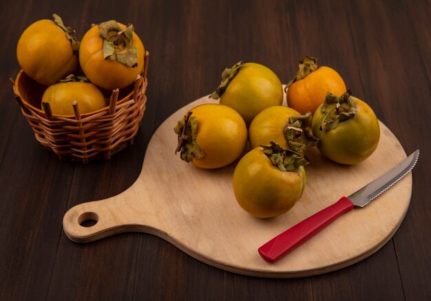 Top view of fresh organic persimmon fruits on a wooden kitchen board with knife on a wooden table