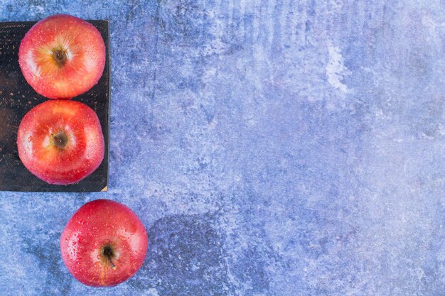 Top view of fresh organic red apples on wooden board over blue.