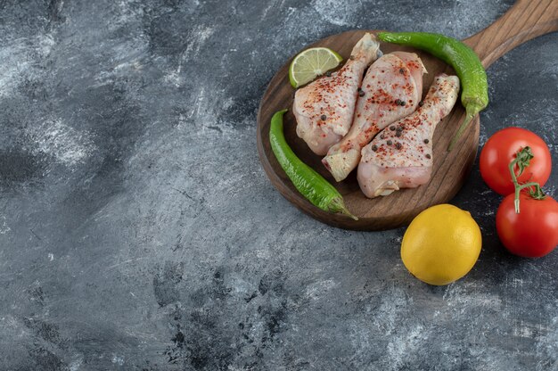 Top view Fresh organic tomatoes and lemon with raw chicken legs over grey background.