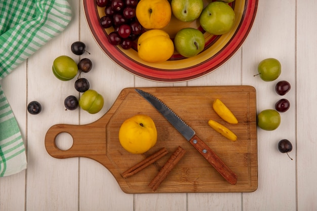 Top view of fresh peach on a wooden kitchen board with knife with cinnamon sticks with fruits isolated on a white wooden background