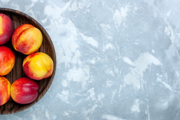 Вид сверху свежие персики, спелые и вкусные фрукты внутри коричневой тарелки на светло-белом столе