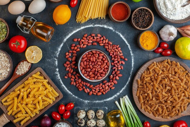 Top view fresh peanuts in circle around eggs vegetables pasta and seasonings on dark background color food raw meal photo health diet