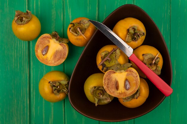 top view of fresh persimmon fruits on a bowl with knife on a green wooden table