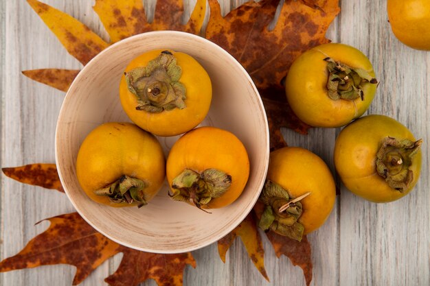 Top view of fresh persimmon fruits on a bowl with leaves on a grey wooden table