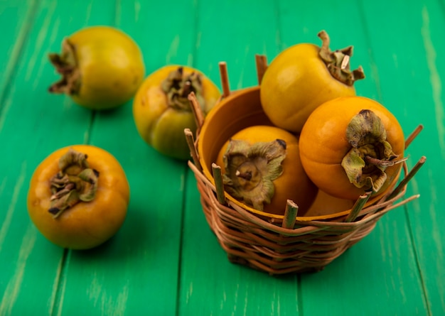 Top view of fresh persimmon fruits on a bucket on a green wooden table