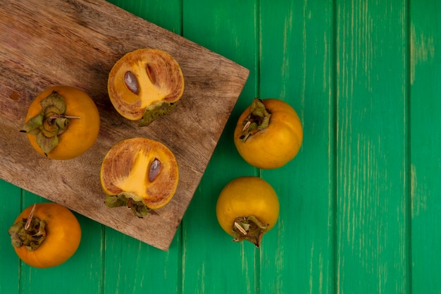 Top view of fresh persimmon fruits on a wooden kitchen board on a green wooden table with copy space