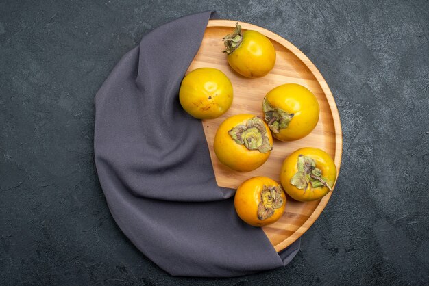 Вид сверху свежей хурмы, спелых сладких фруктов на темном столе, спелых фруктов