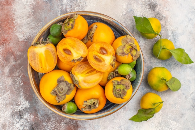 Top view fresh persimmons feykhoas in a big bowl and mandarines on nude background