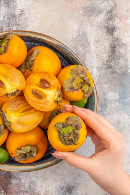 Free photo top view fresh persimmons feykhoas in a bowl persimmon in female hand on nude background