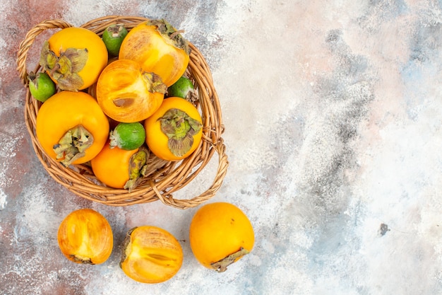 Top view fresh persimmons feykhoas in wicker basket and persimmons on nude background