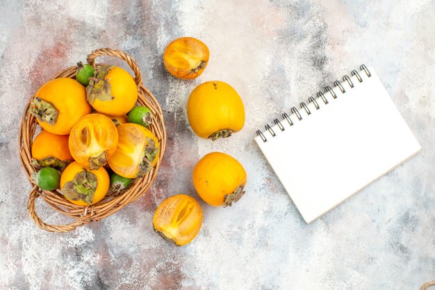 Top view fresh persimmons in wicker baske tpersimmons a notepad on nude background