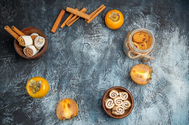 Top view of fresh persimmons with confitures and cinnamon on dark surface