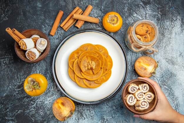 Top view of fresh persimmons with confitures and cinnamon on dark surface