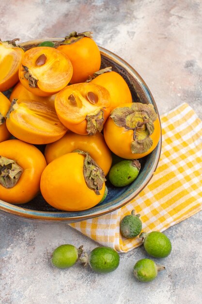 Top view fresh persimmons in a wooden bowl yellow kitchen towel feykhoas on nude background