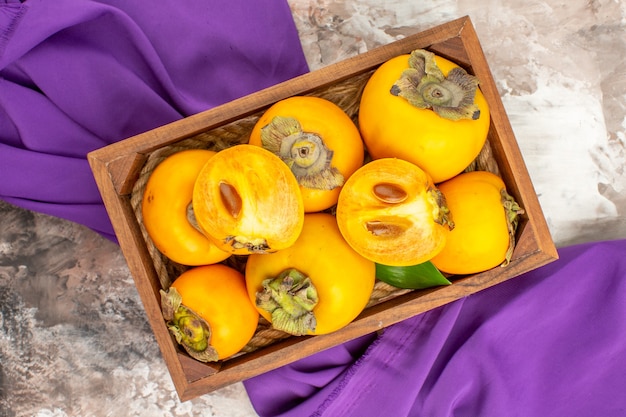 Top view fresh persimmons in wooden box on purple shawl on nude background