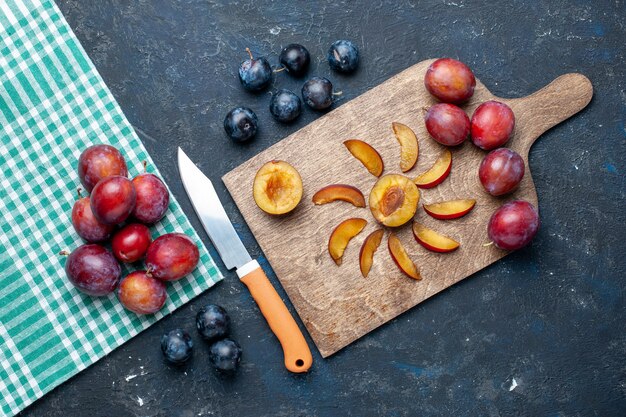 top view of fresh plums whole mellow and juicy sliced on dark desk, fruit vitamine summer