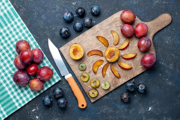 Vista dall'alto di prugne fresche intere morbide e succose affettate sulla scrivania grigio-scuro, frutta fresca vitamina estate